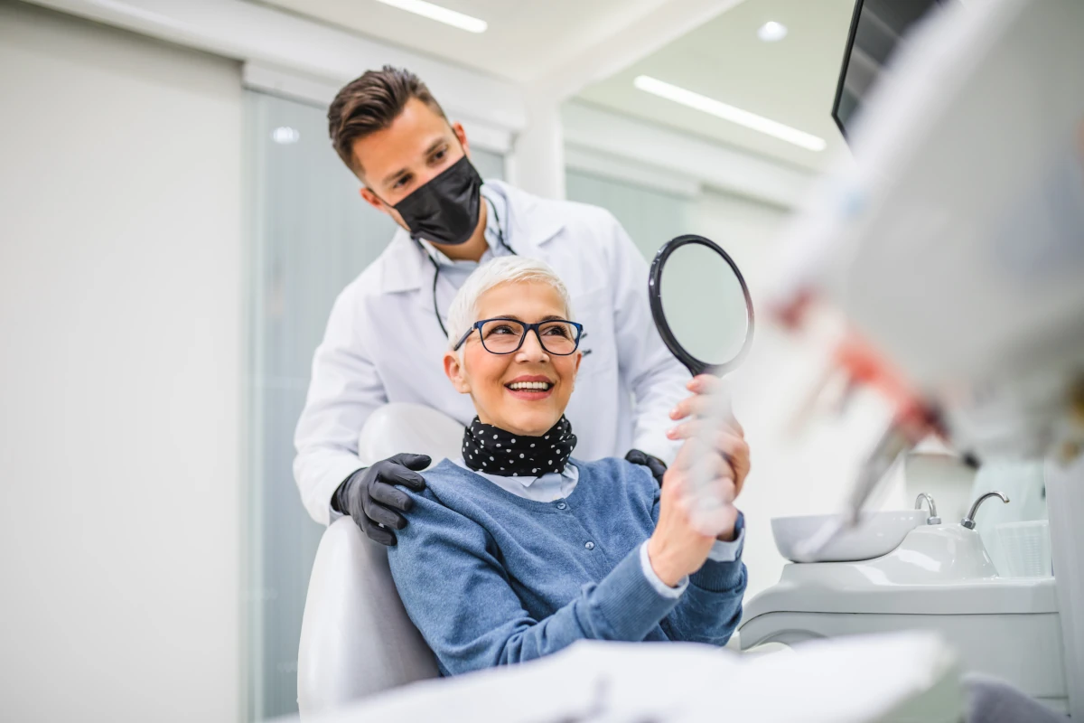 Dentist standing behind patient inspecting their smile with a mirror